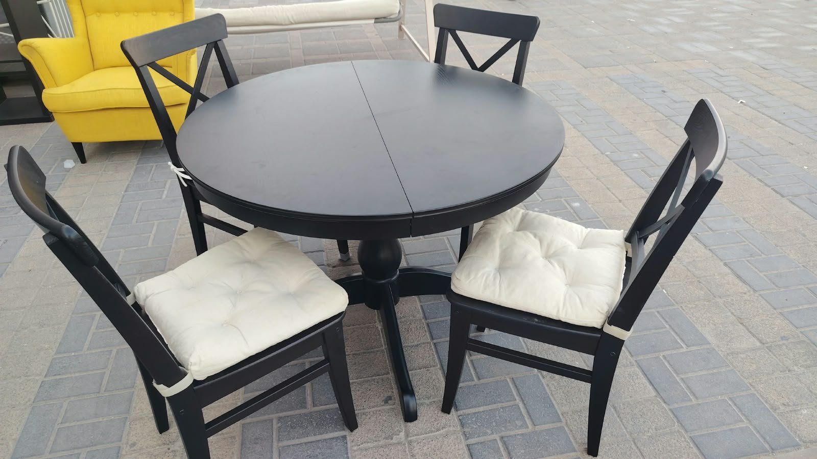 Modern black round extendable dining table set with 4 cross-back chairs and cream cushions at Fairy of Fortune Used Furniture Abu Dhabi