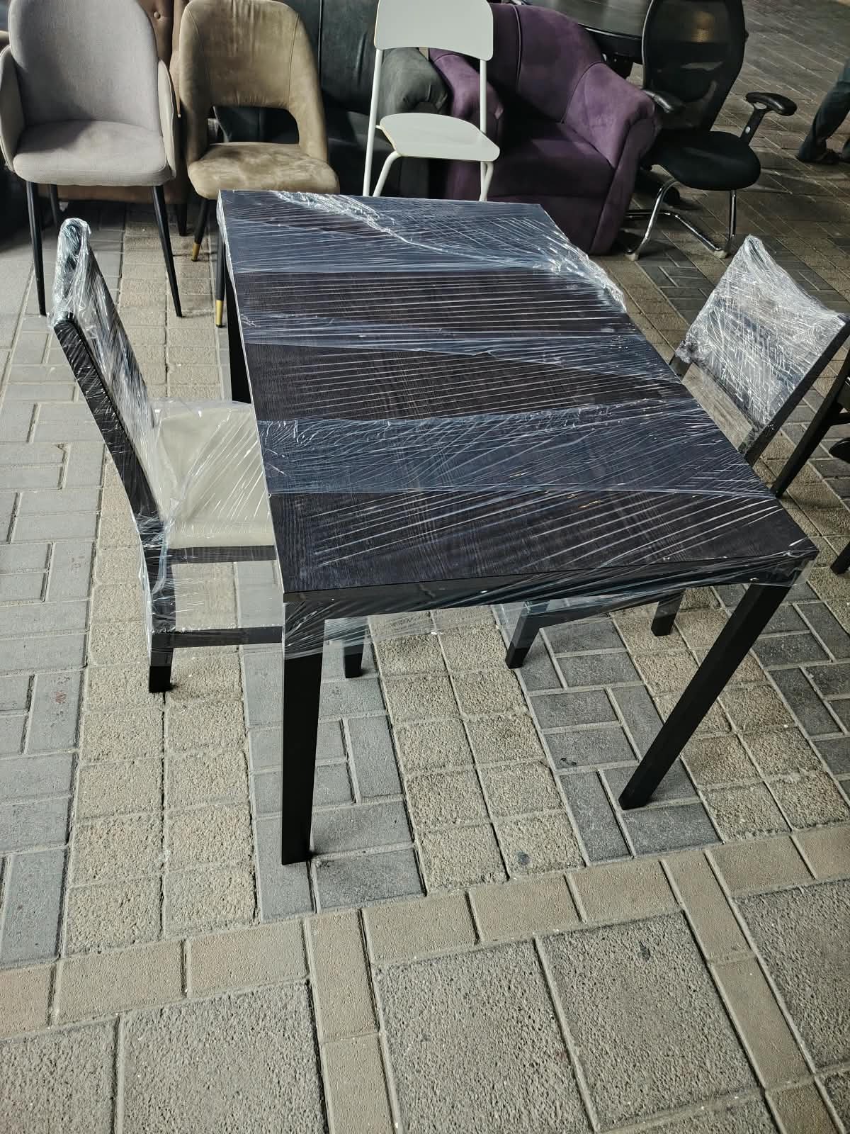 Modern dark wood rectangular 2-seater dining table wrapped for protection with two matching cushioned chairs at Fairy of Fortune Used Furniture Abu Dhabi