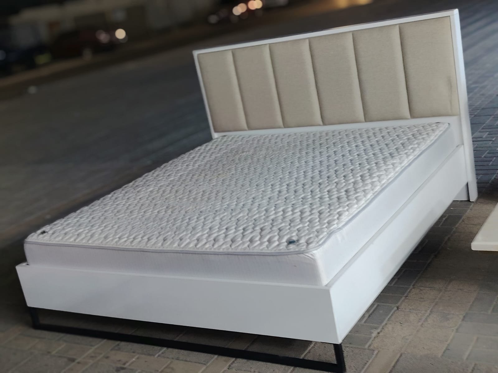Modern white wooden double bed frame featuring a beige vertical channel-tufted upholstered headboard and plush comfortable mattress at Fairy of Fortune Used Furniture Abu Dhabi